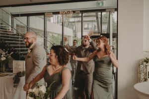 Wedding party members in olive green dresses celebrate in a modern indoor venue.