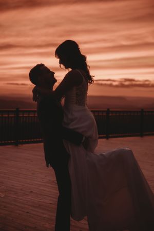 Romantic silhouette of newlyweds embracing on a deck during sunset.