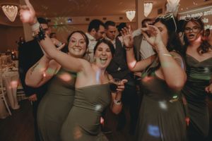 Wedding party in olive green dresses dancing and celebrating at the reception.
