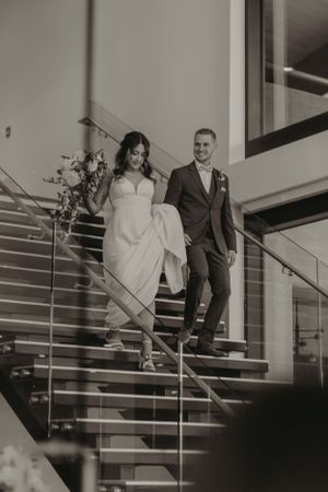 A couple descending modern stairs in formal wedding attire.