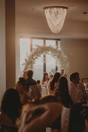 A wedding reception with a floral arch and elegant chandelier illuminating the celebration.