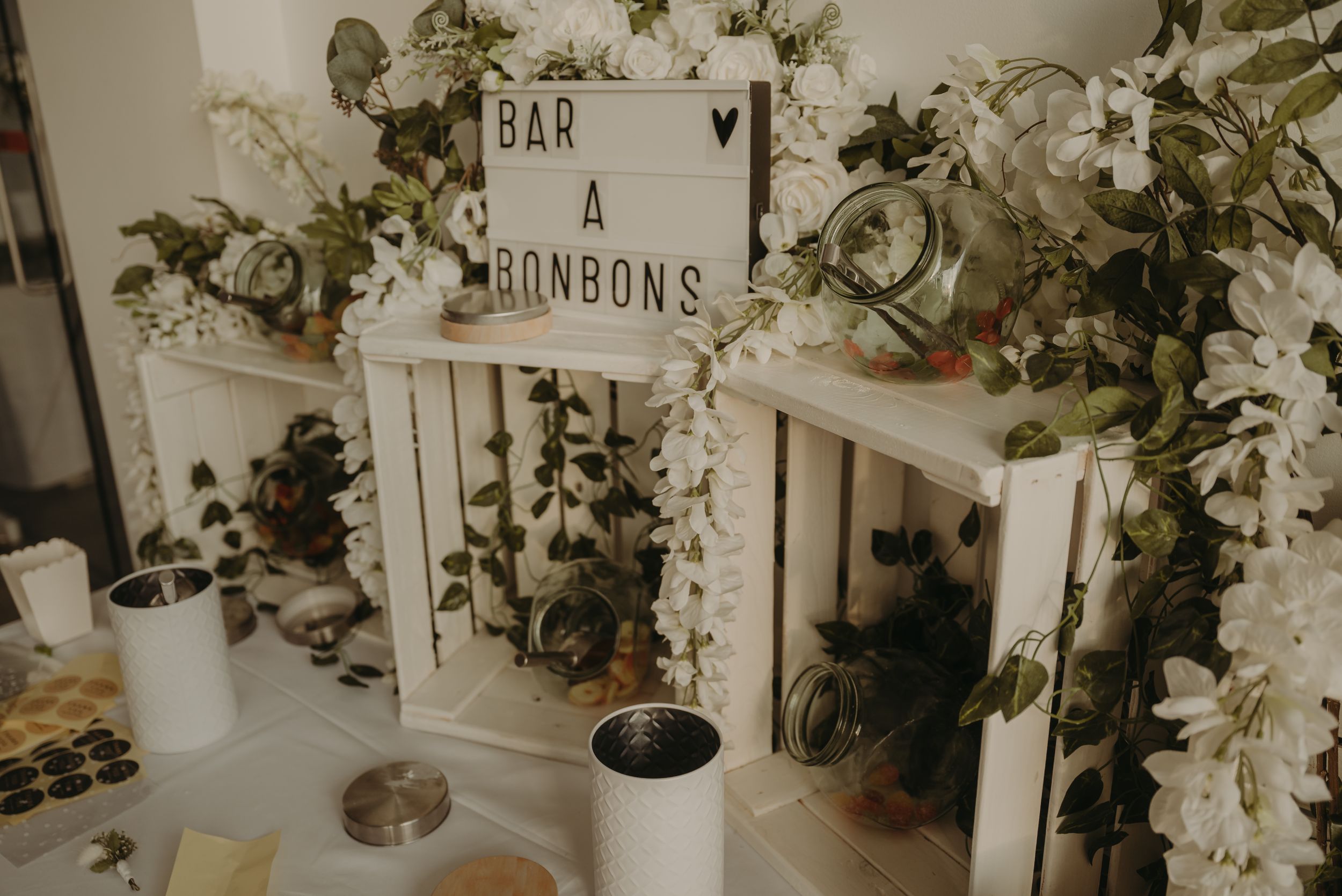 Wedding reception decor featuring rustic bar and rainbows sign with floral arrangements.