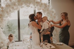 An intimate family moment during a wedding reception under a white floral arch.