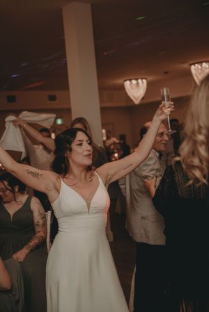 Wedding reception guests enjoy dancing and celebrating with raised glasses under decorative heart-shaped lighting.