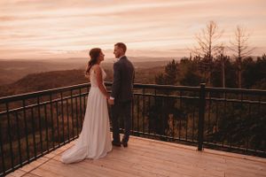 Wedding couple standing together on mountain viewing deck during golden hour.