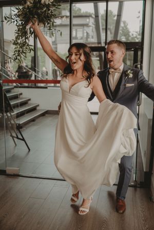 A joyful couple dancing at their wedding reception, with the bride in white and groom in gray suit.