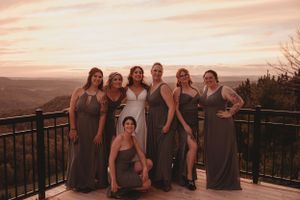 Wedding party in matching dresses posing together on mountain overlook at sunset.