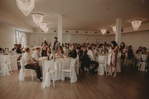 Wedding reception venue with elegant crystal chandeliers and white-clothed tables filled with guests.