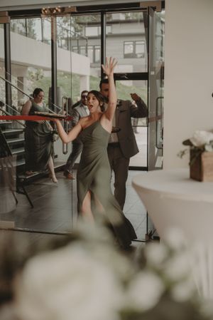Wedding party dancing and celebrating in a modern venue with glass walls and staircase.
