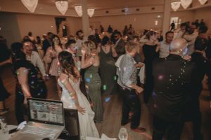 Crowded dance floor at a wedding reception with DJ booth and heart-shaped lighting fixtures.