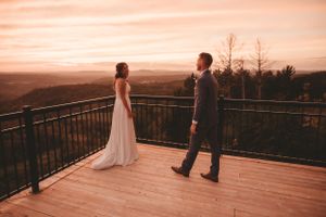 Couple sharing romantic moment on wooden deck overlooking mountain landscape at sunset.