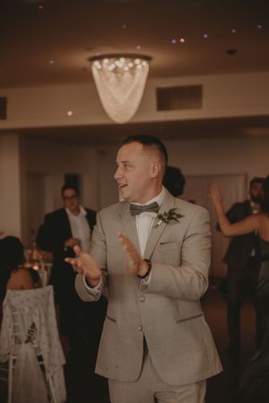 Wedding guest in light grey suit celebrating on dance floor under crystal chandelier.
