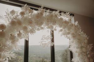 White floral arch with 'Better Together' text displayed against a window with scenic view.