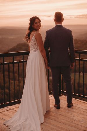 Elegant wedding portrait on mountain deck with bride's dress trailing in sunset light.