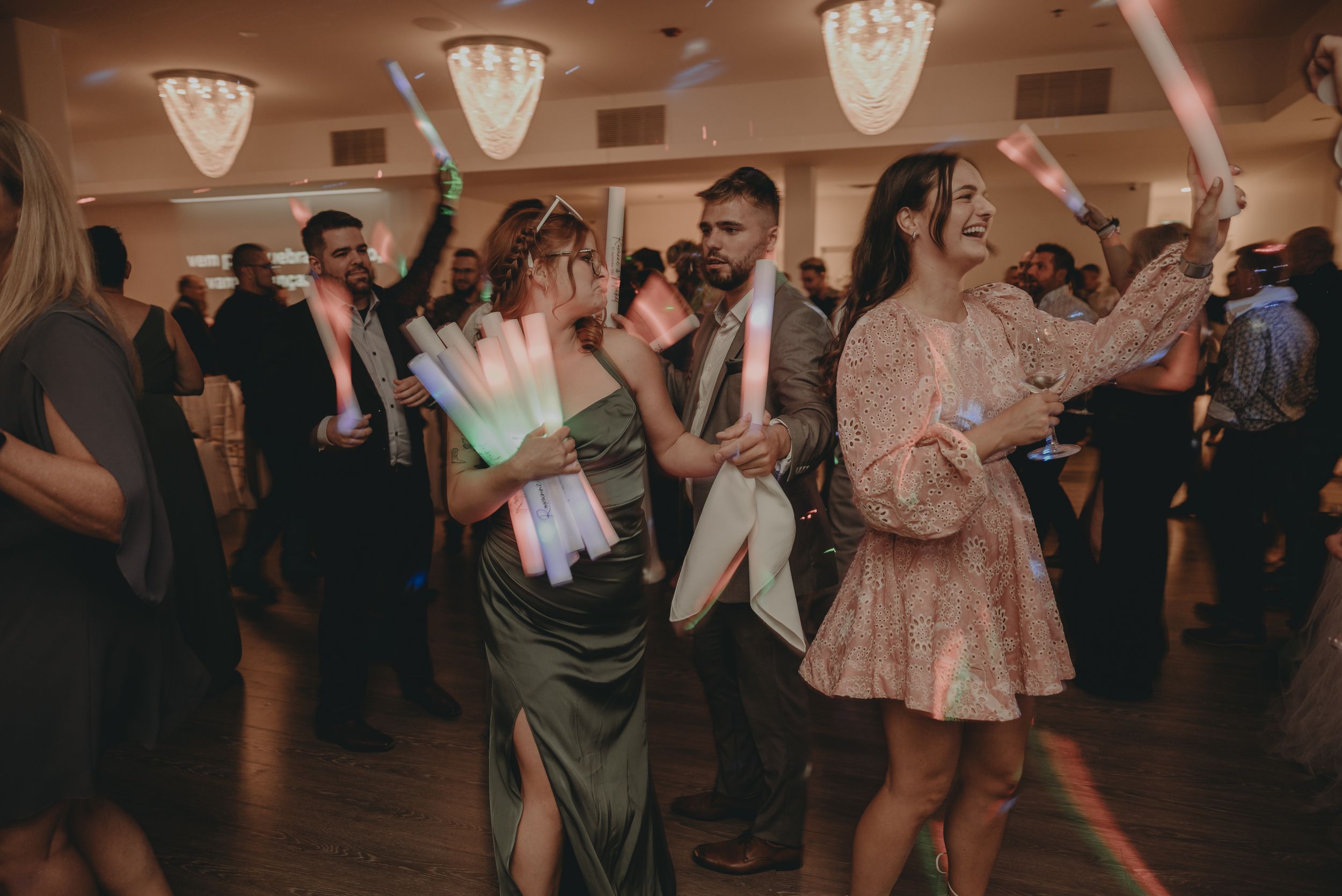 Wedding guests dancing in formal attire under warm lighting at an indoor reception.