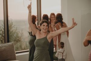 Wedding party guest in olive green dress celebrating with raised arms at reception.