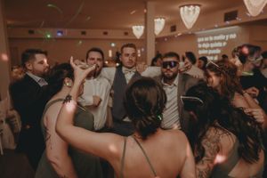 Wedding guests dancing and celebrating at an indoor reception under ambient lighting.