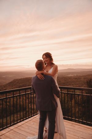 A romantic embrace between newlyweds on a scenic mountain deck at dusk.