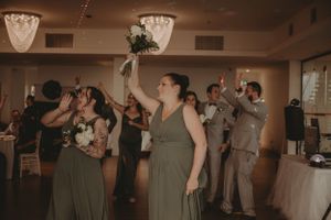 Wedding party members dancing with raised arms under vintage ceiling lights.