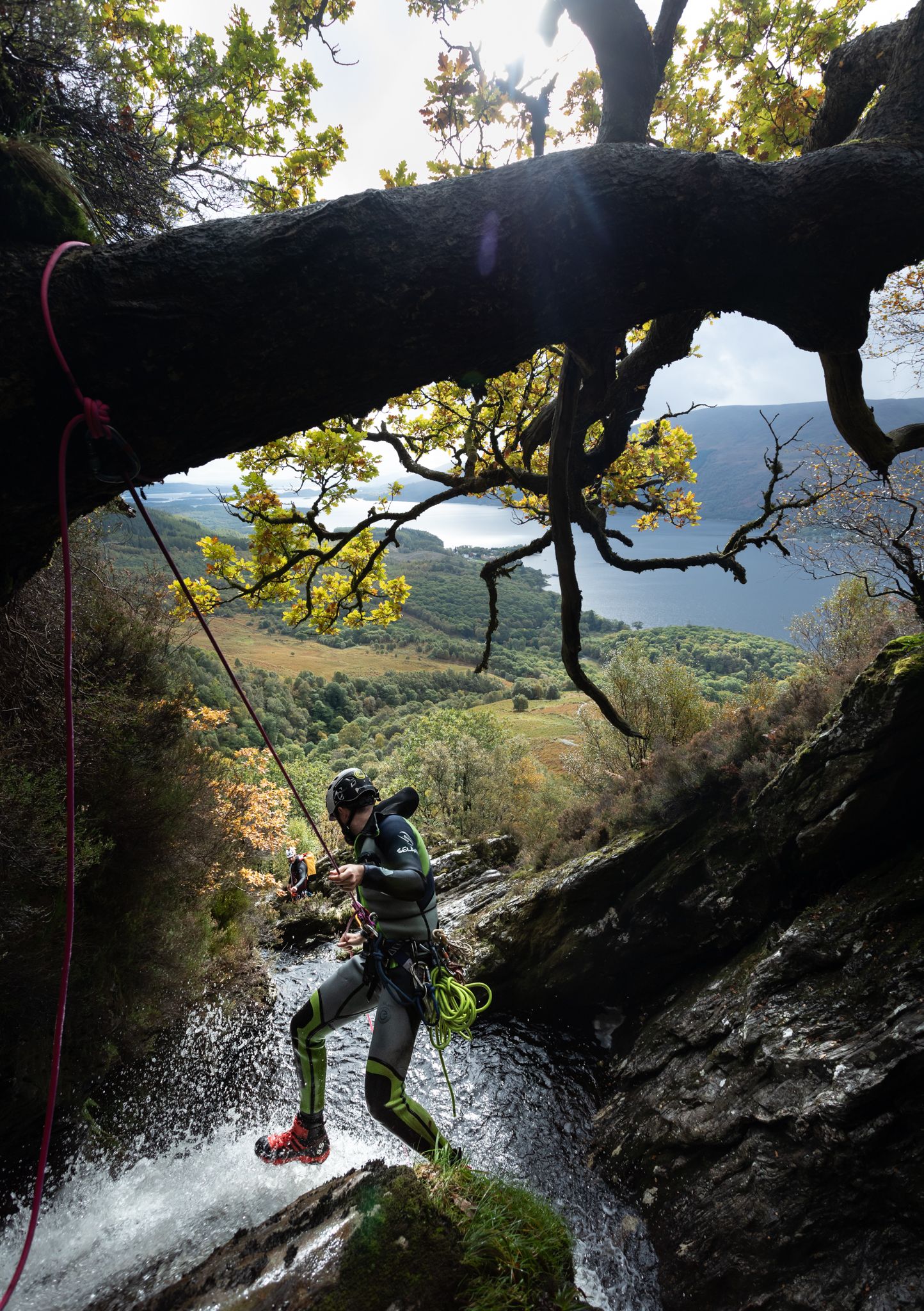 Adventure seekers rappel down a waterfall while canyoneering through a scenic mountain gorge on a sunny day above Loch Lomond in Scotland