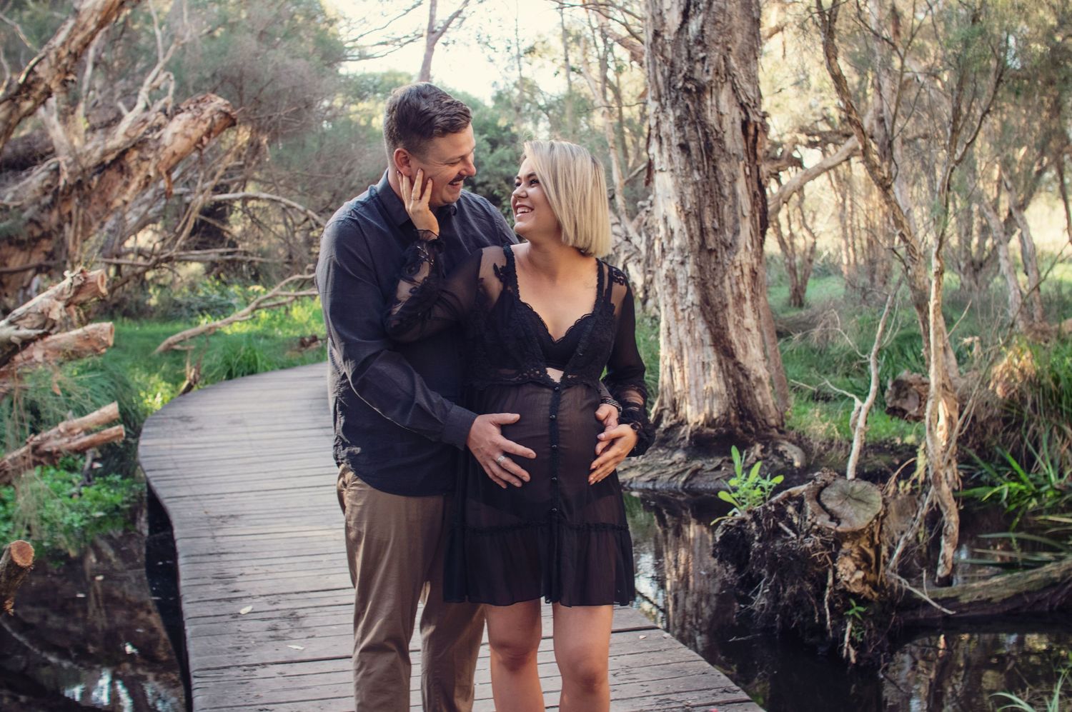 couple smiling and touching pregnant belly outside