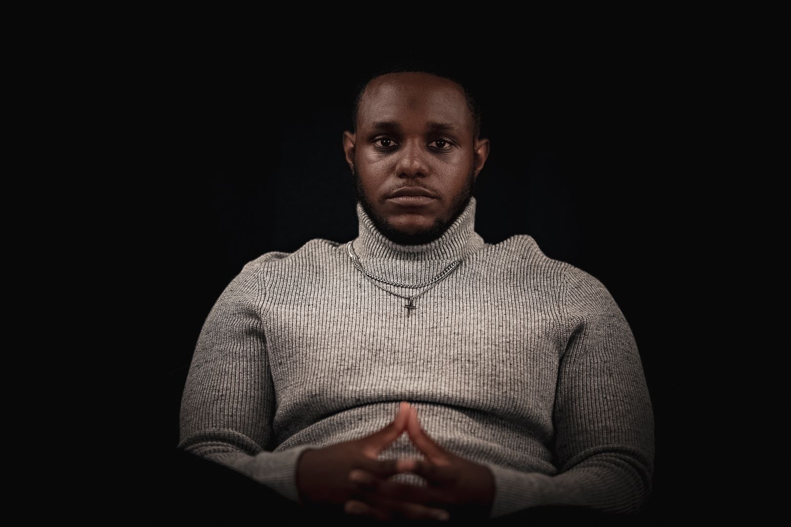 Professional portrait against dark background showing contemplative pose in gray turtleneck sweater.