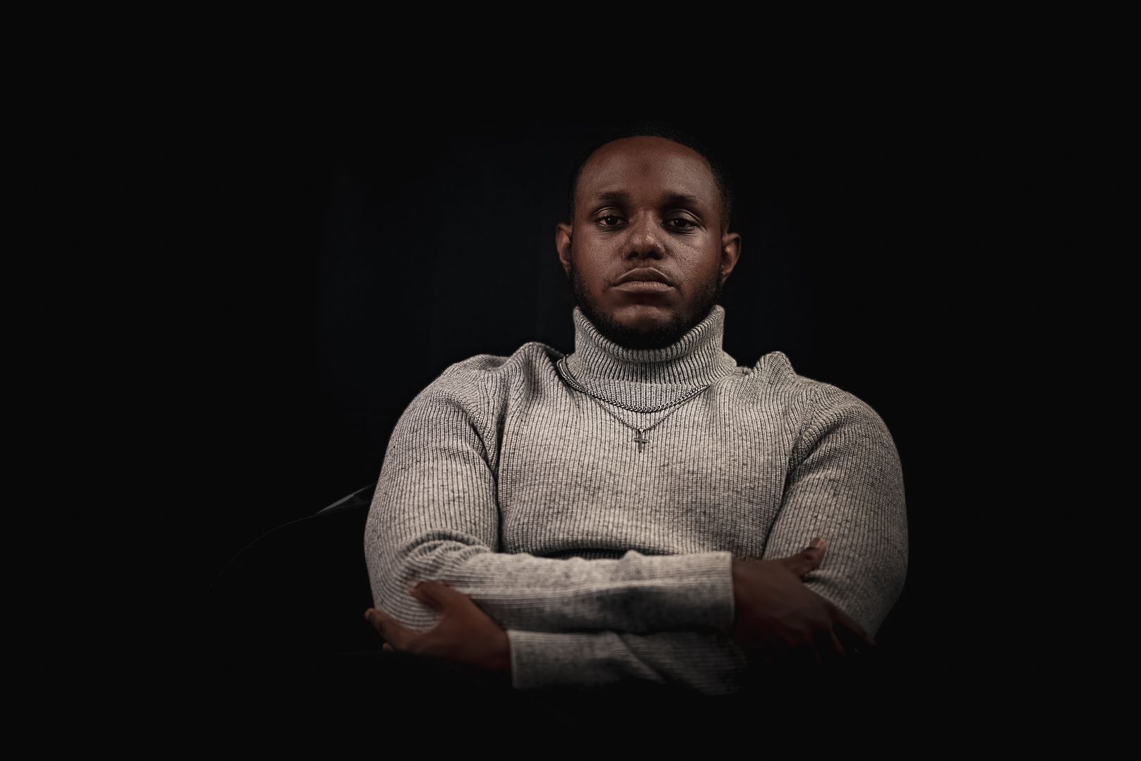 Artistic portrait with crossed arms in turtleneck against dark background showing confidence.