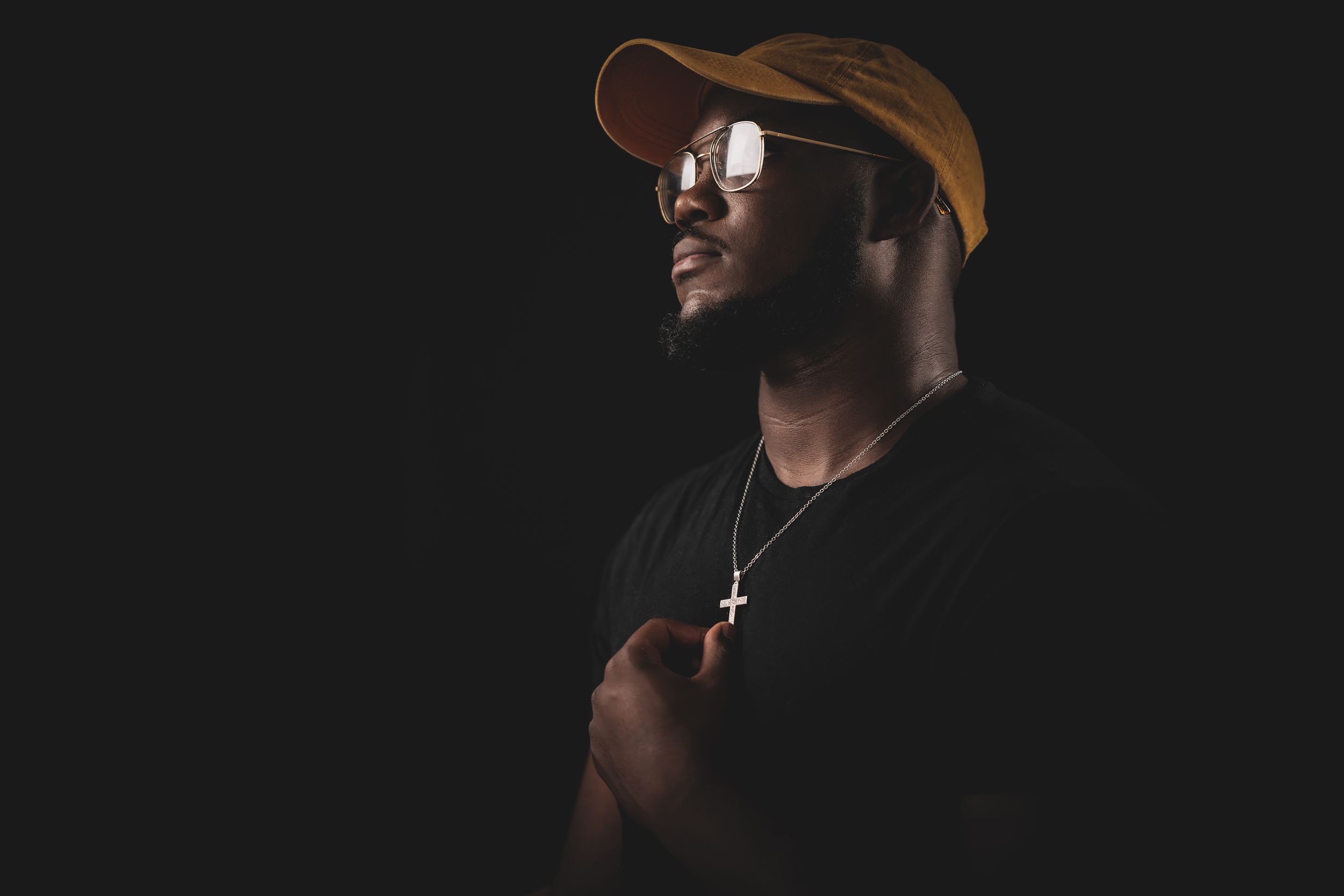 Dramatic portrait of person in brown cap and sunglasses against dark background.