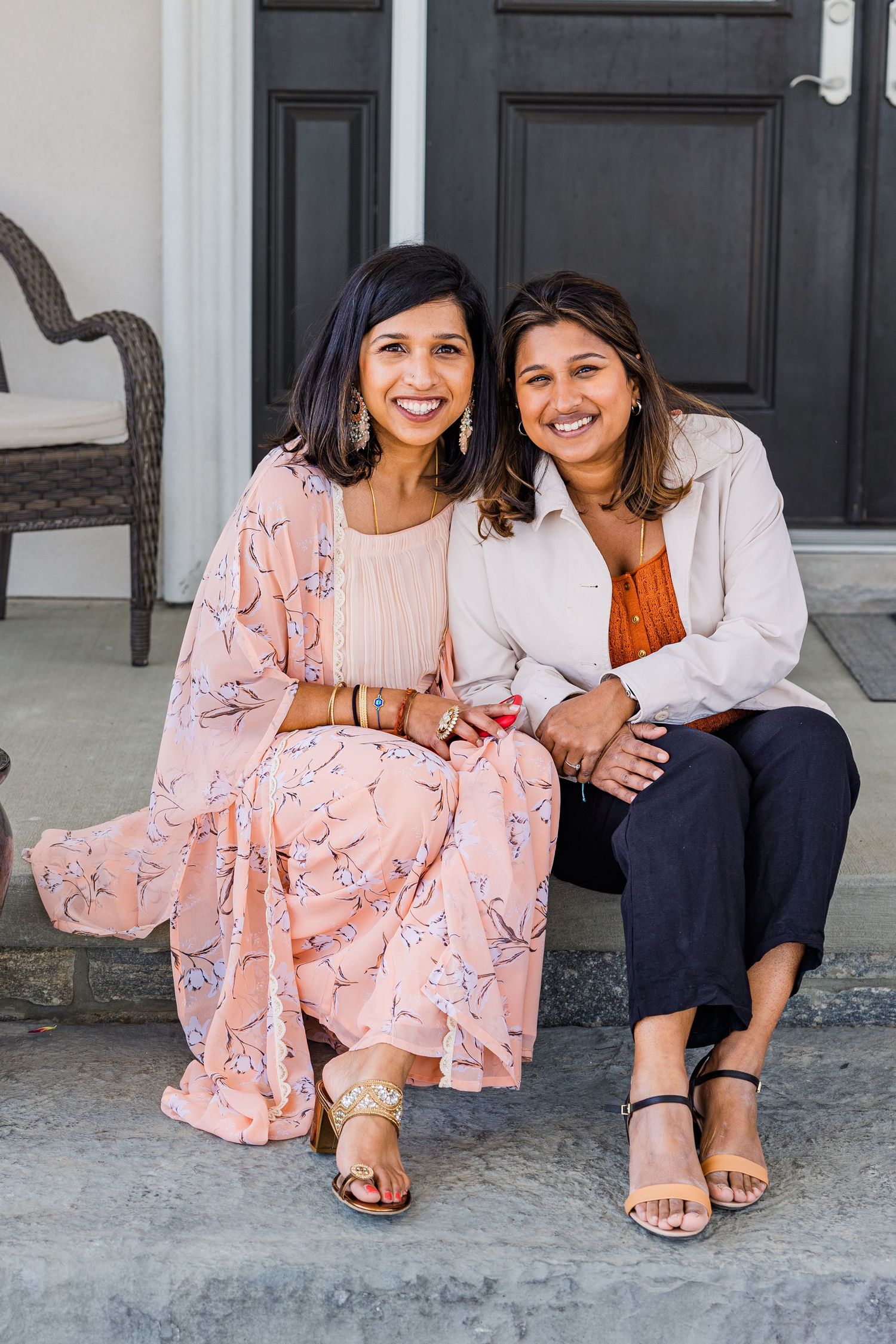 Two women sitting together on porch steps wearing pink floral and orange outfits.