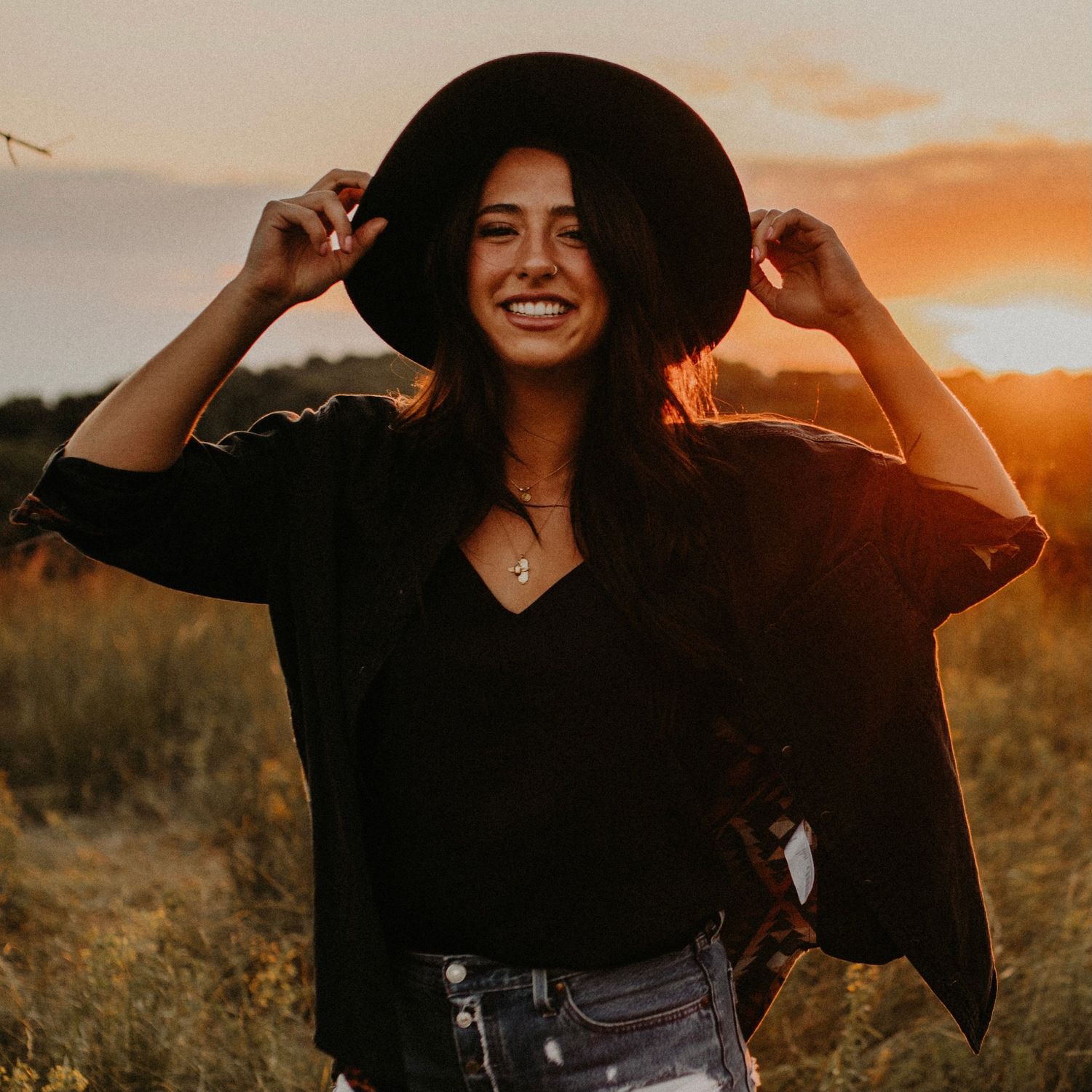 Person adjusting wide brim hat during golden hour portrait session.