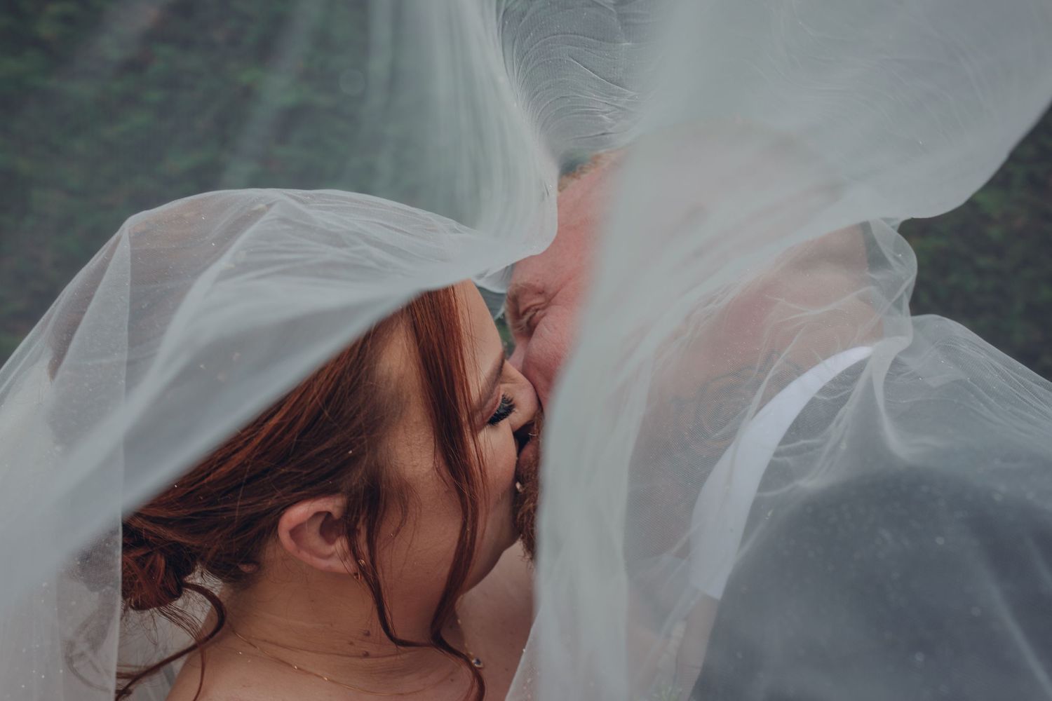 Close-up artistic shot of a bride underneath flowing white veil fabric.
