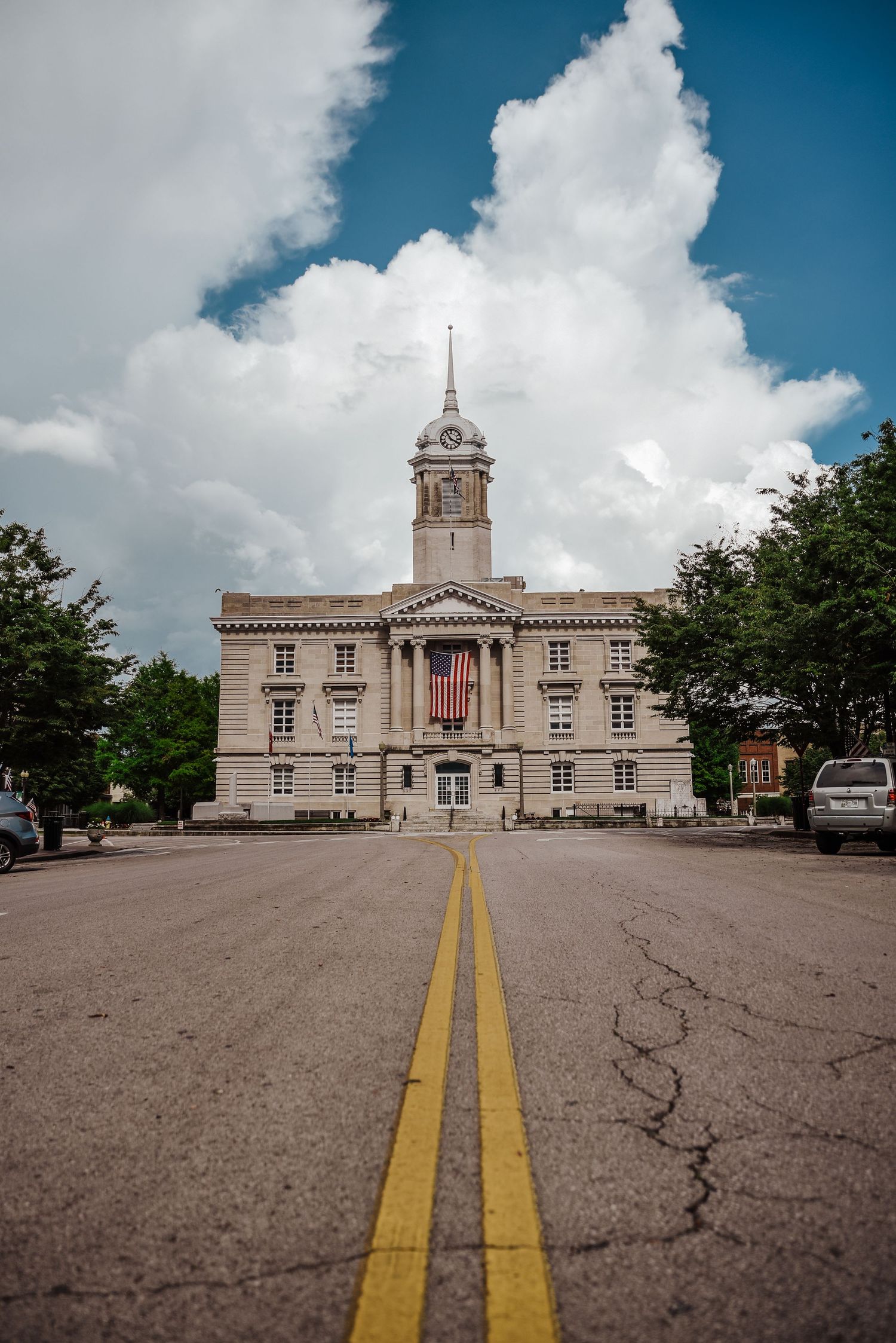 Classic government building with American flag and double yellow road lines leading to entrance.