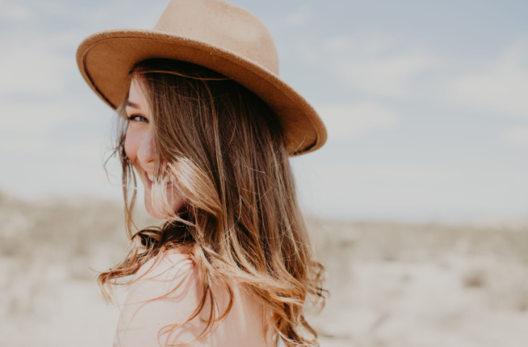 Close-up shot of someone wearing a brown wide-brimmed hat in desert scenery.