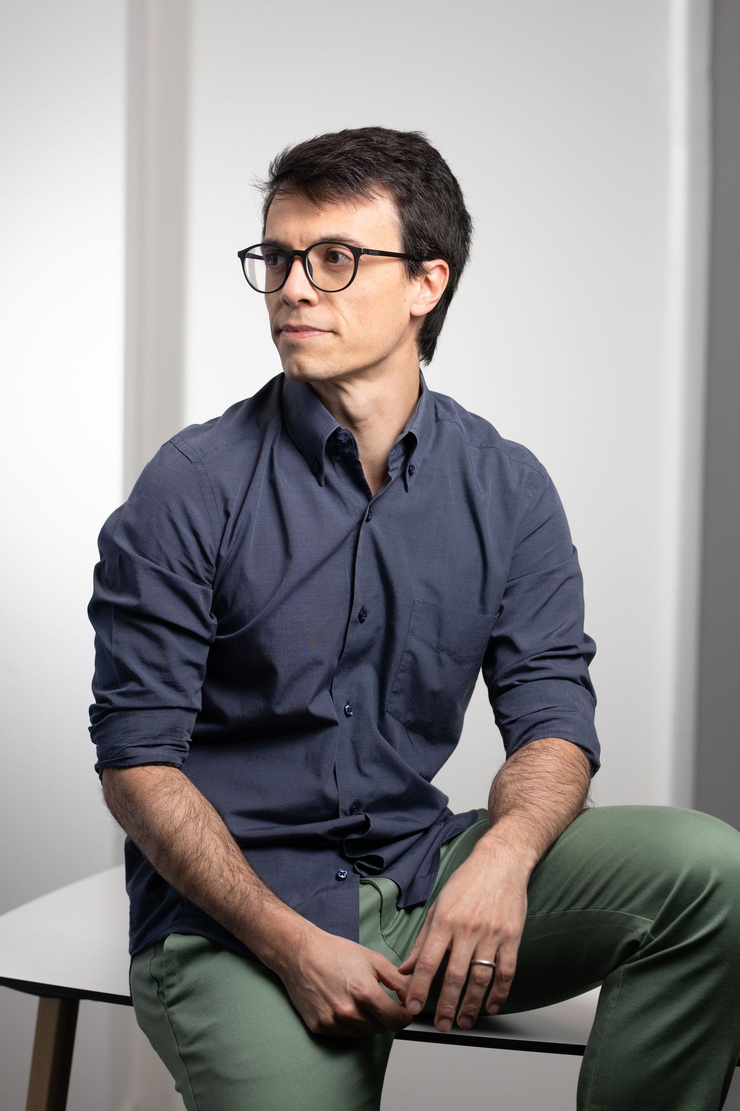Professional portrait of a person wearing glasses and a dark button-down shirt while sitting casually.