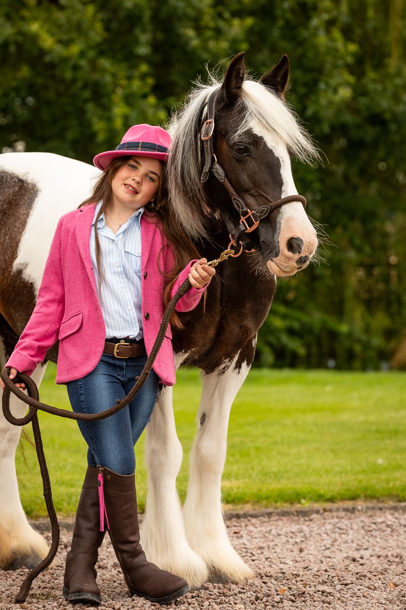 A black and white draft horse stands with a pink-clad equestrian on a dirt path surrounded by greenery.