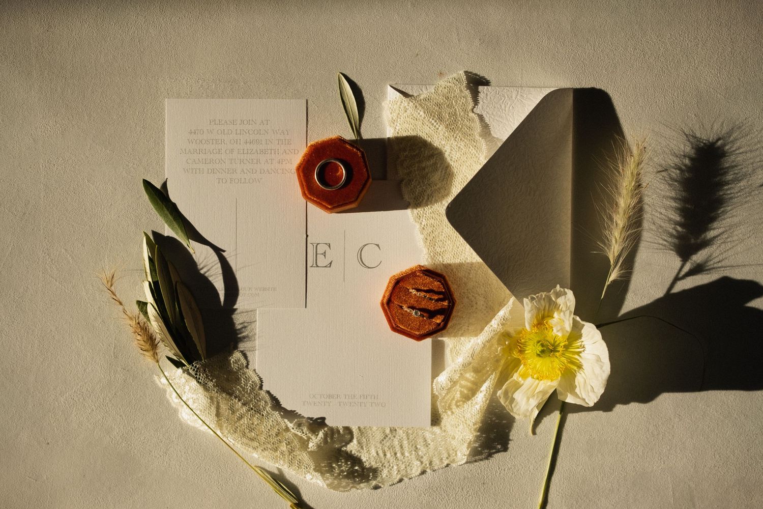 Wedding invitations and decorative feathers arranged artistically on a neutral background.