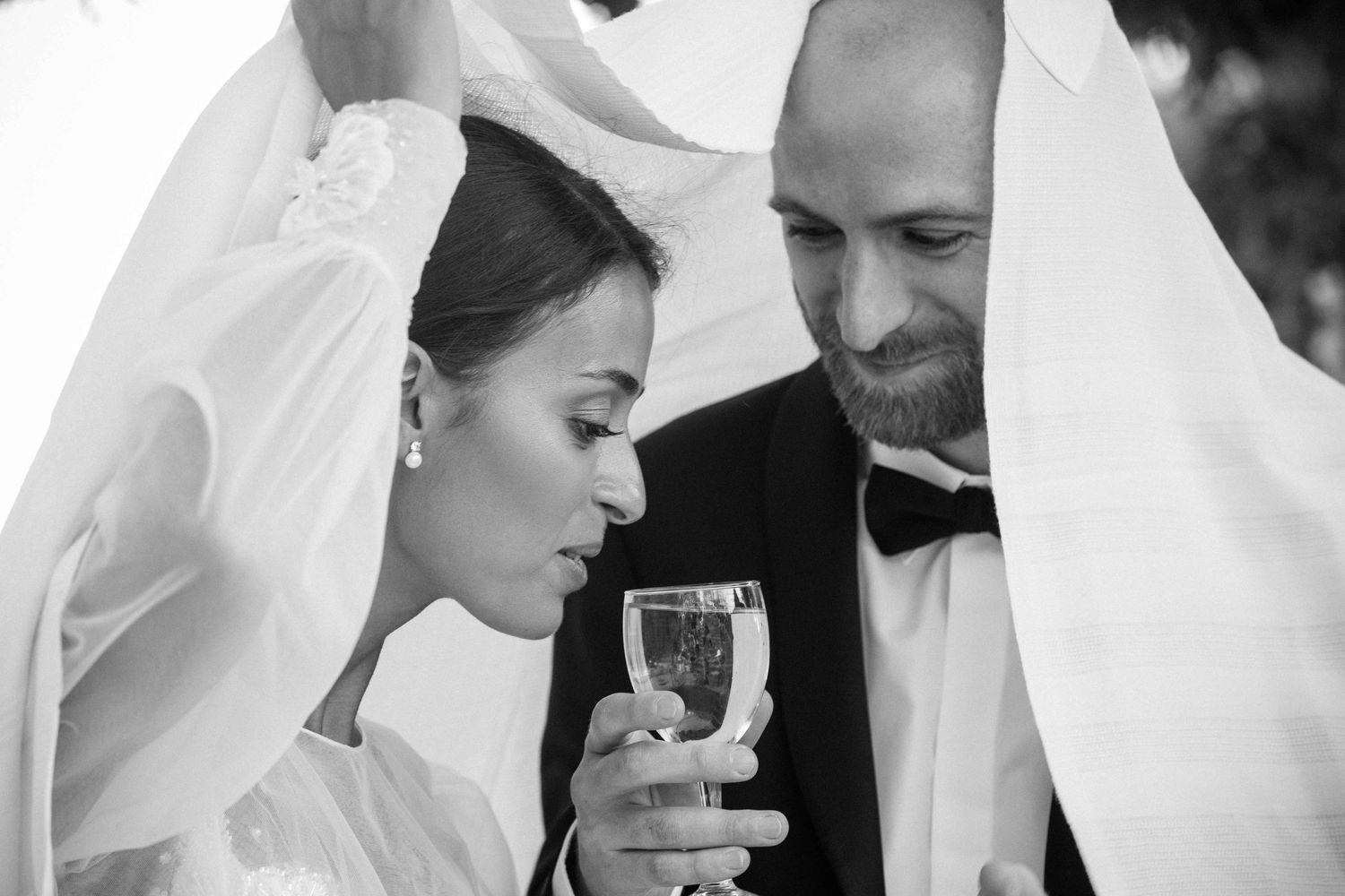 Black and white photo of a tender wedding moment shared over a champagne glass.