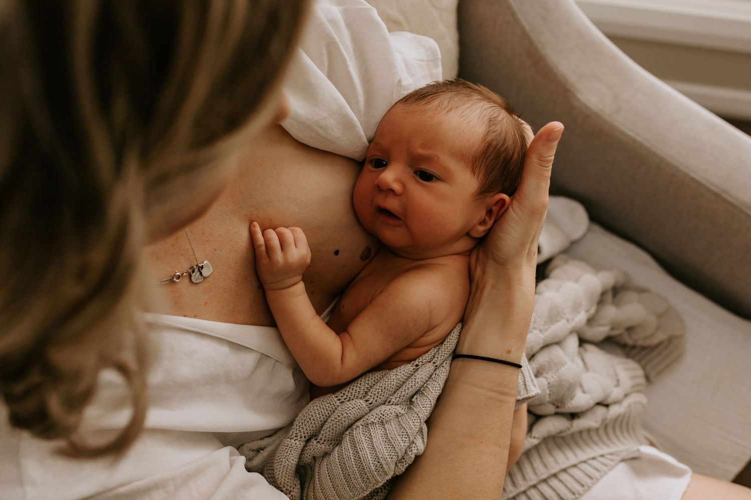 Baby rests on white bedding while being comforted during an intimate indoor photography shoot.