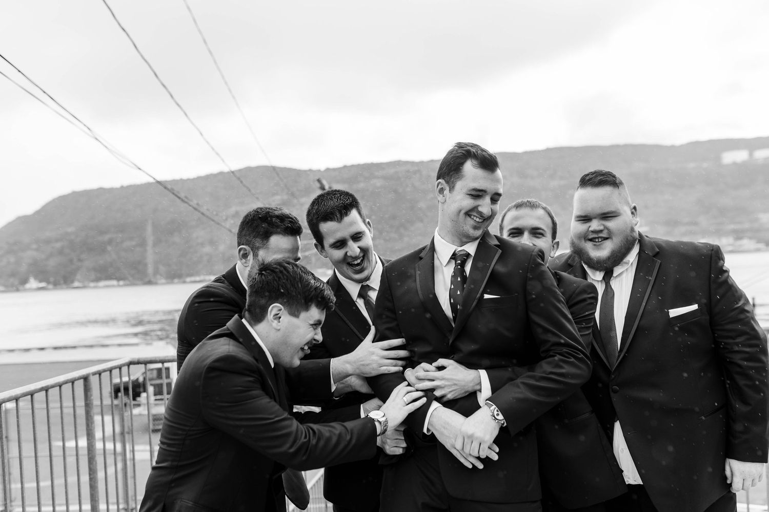 Groomsmen share laughs together on a seaside balcony wearing matching formal attire.