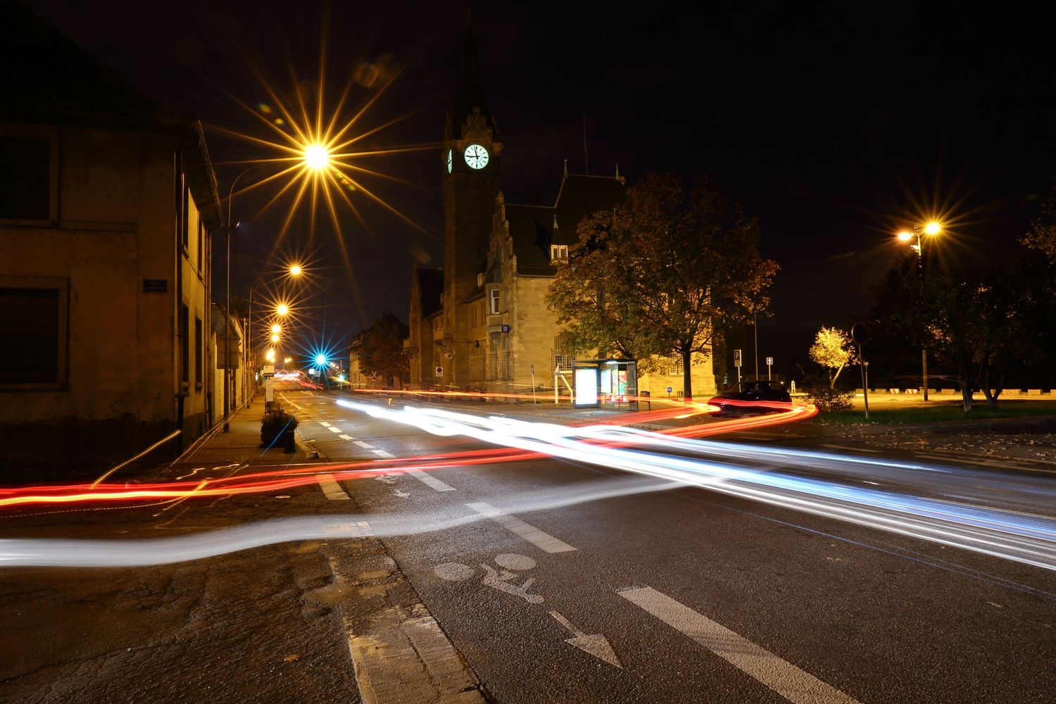 Light trails from cars intersect at a nighttime street crossing.