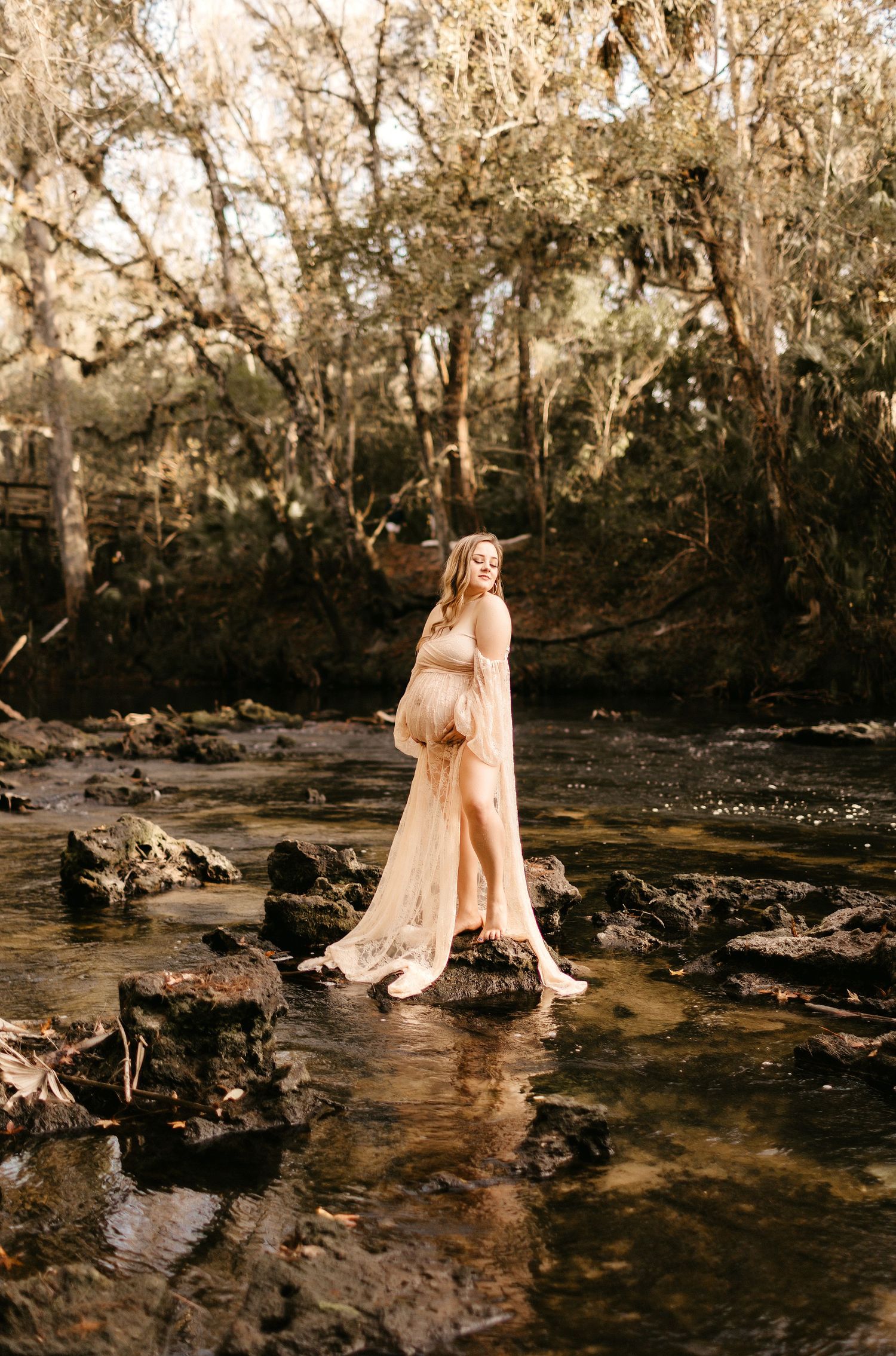 a pregnant mom stands on rocks in Hillsborough river holding her belly while posing for a photo
