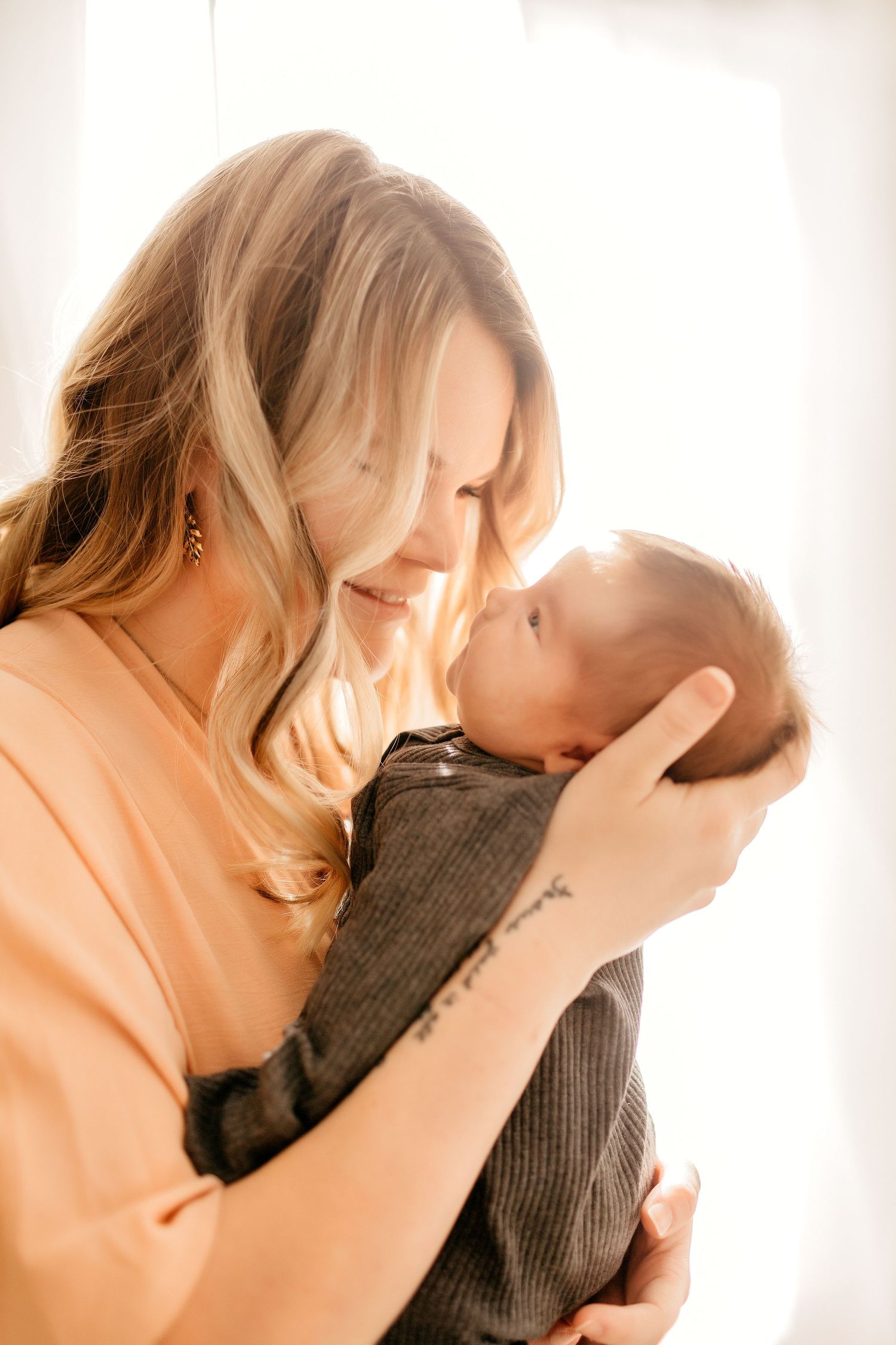 a mom is holding her newborn up to her face smiling with their noses touching while posing for a photo