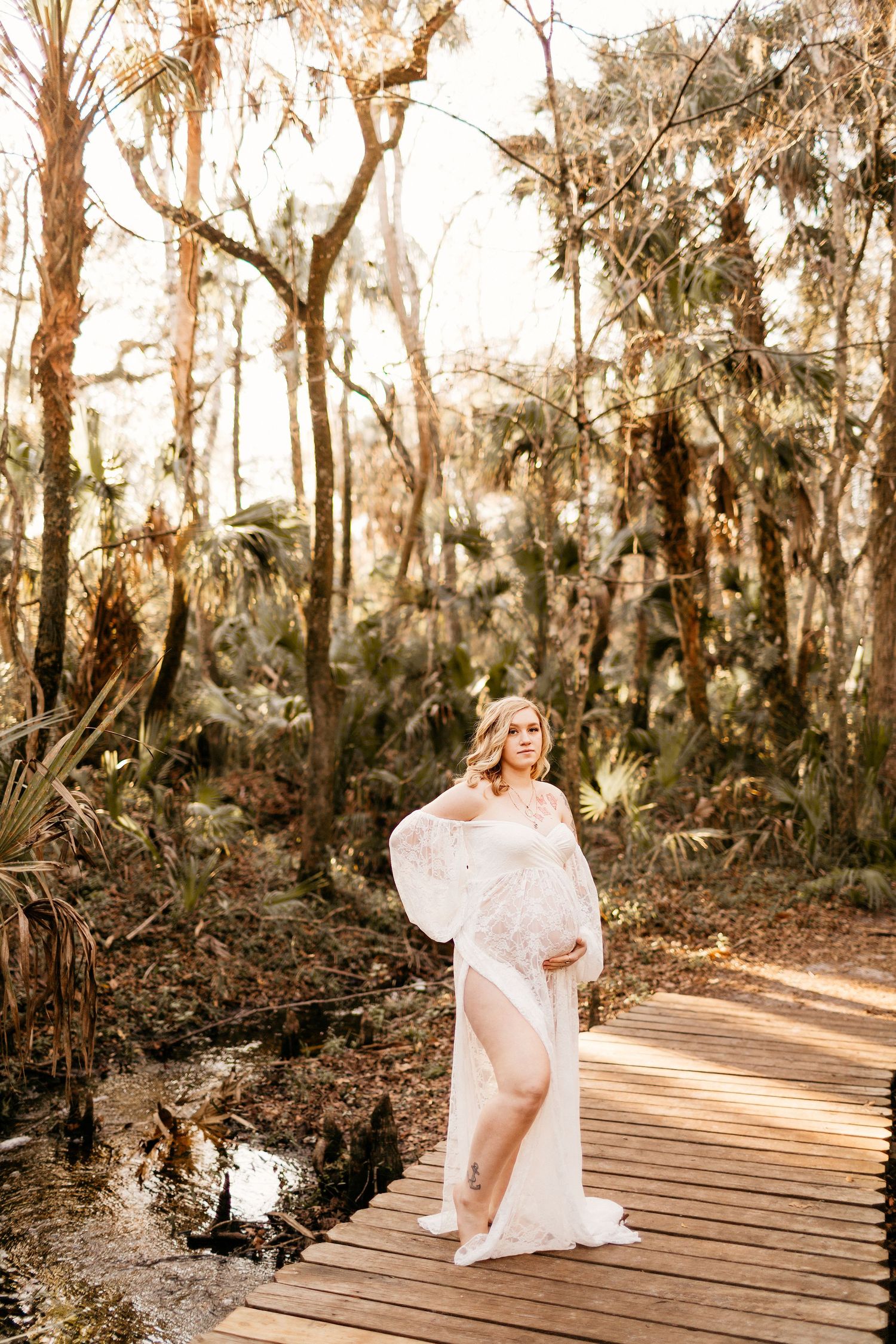 a pregnant mom has one hand on her belly and one on her lower back while posing for a photo