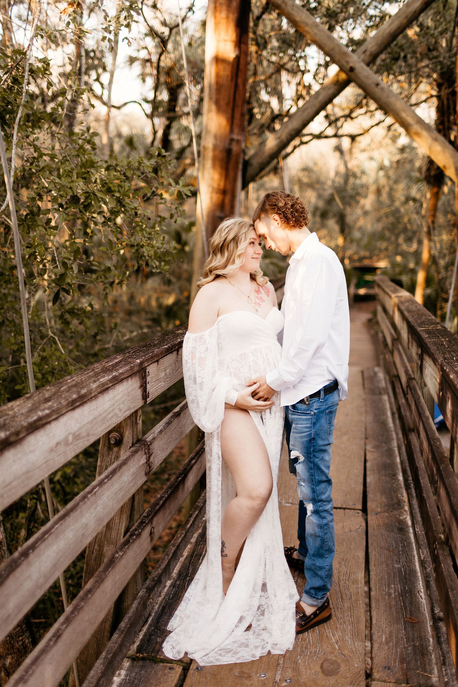 a pregnant couple stands with their foreheads together and hands on her belly while posing for a photo