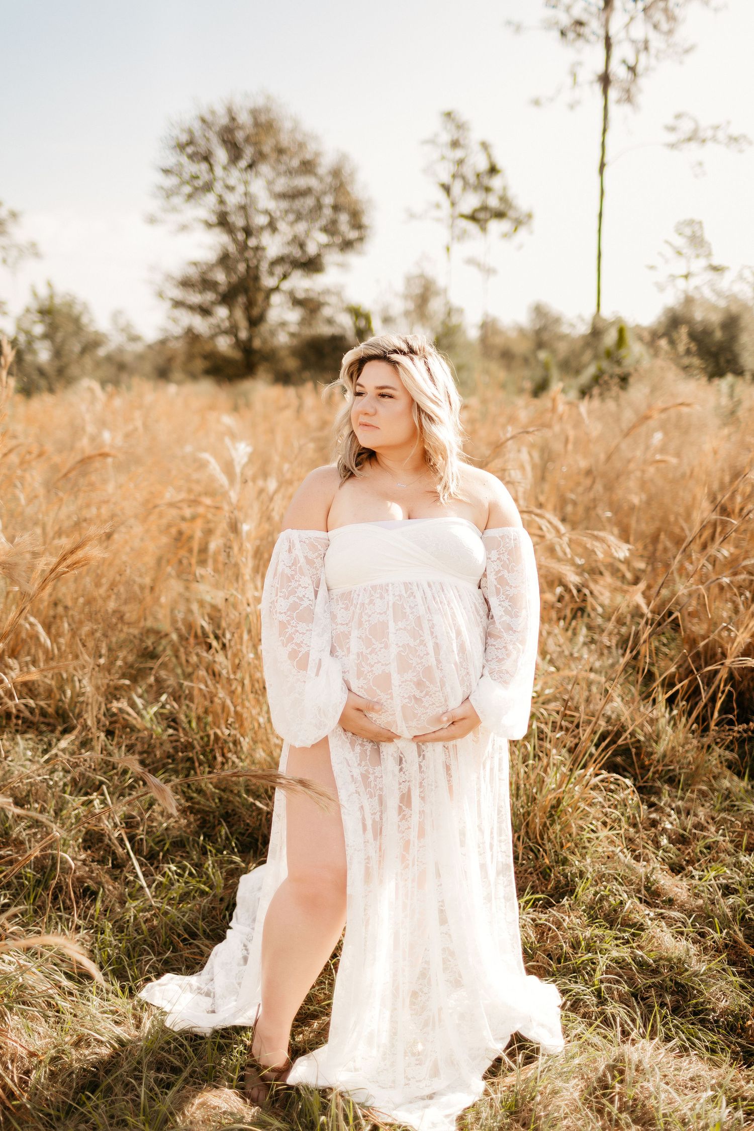 a pregnant mom stands holding her belly and looking to the side while posing for a photo
