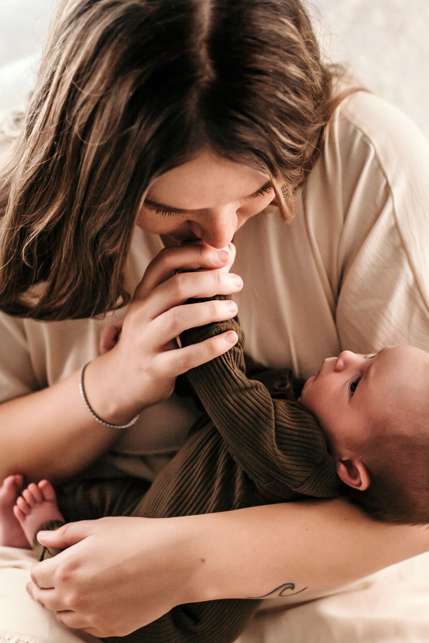 a mom is holding her baby and has his hand in hers kissing it