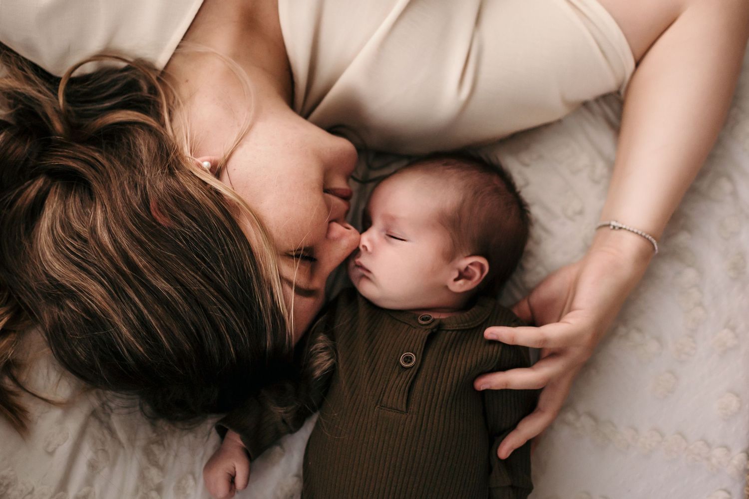 a mom and her baby lay on a bed with their eyes closed
