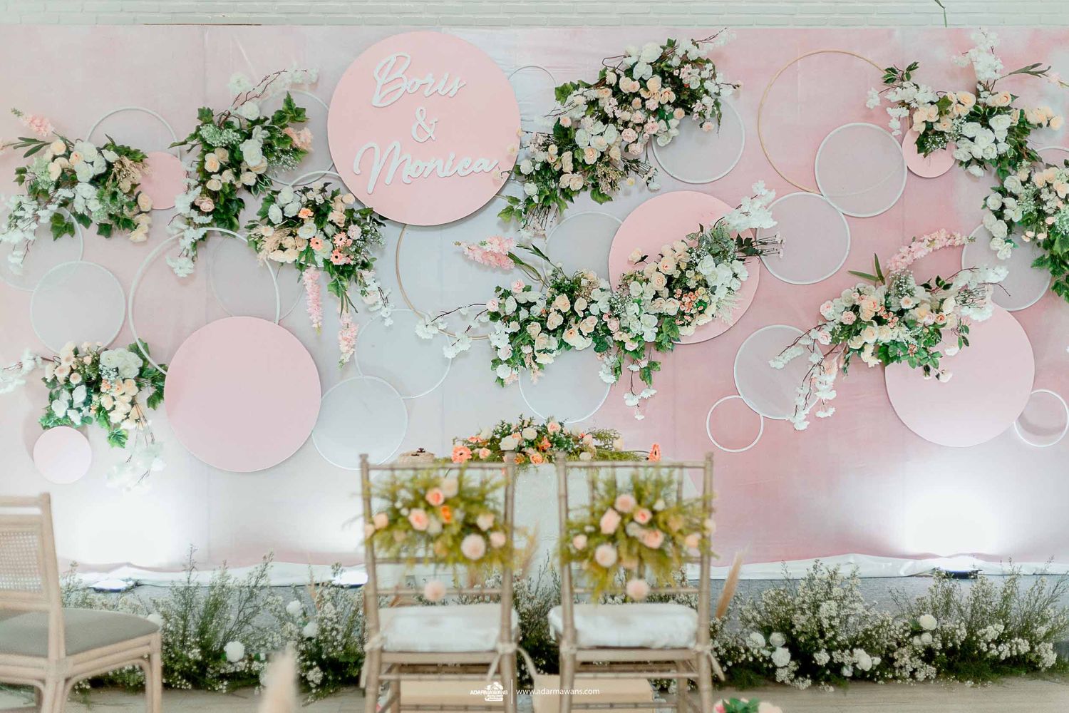 Modern wedding reception setup with pink circles and white floral arrangements against a pastel backdrop.