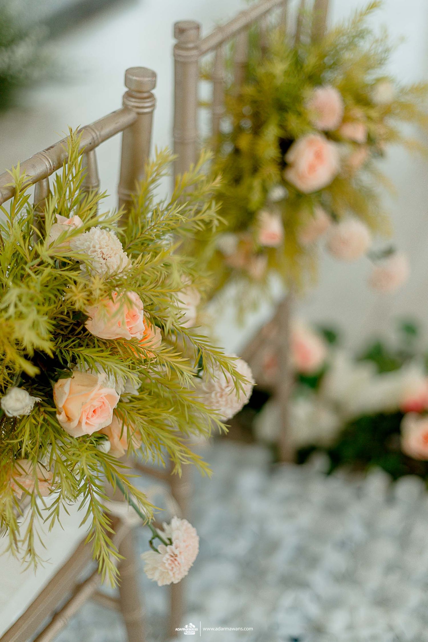 Elegant floral arrangement with pink roses and greenery adorning a chair at a wedding ceremony.