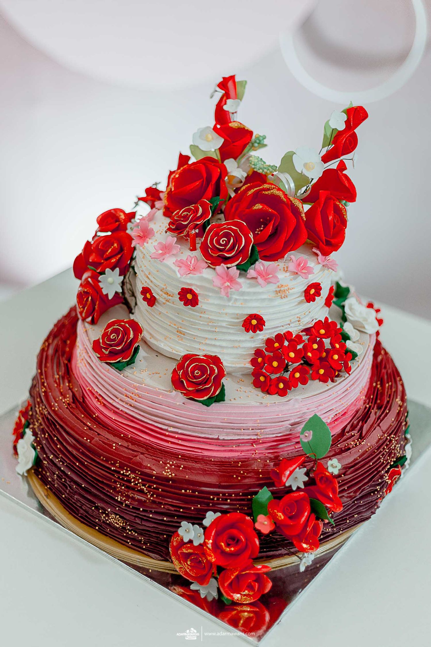 Three-tiered ombre wedding cake decorated with cascading red roses and white details.